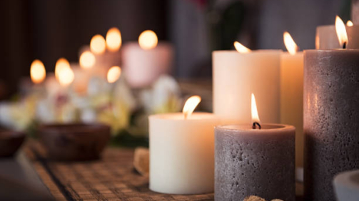 Closeup of burning candles spreading aroma on table in a spa room. Beautiful composition with grey and white candles for spa treatment. Zen and relax concept.